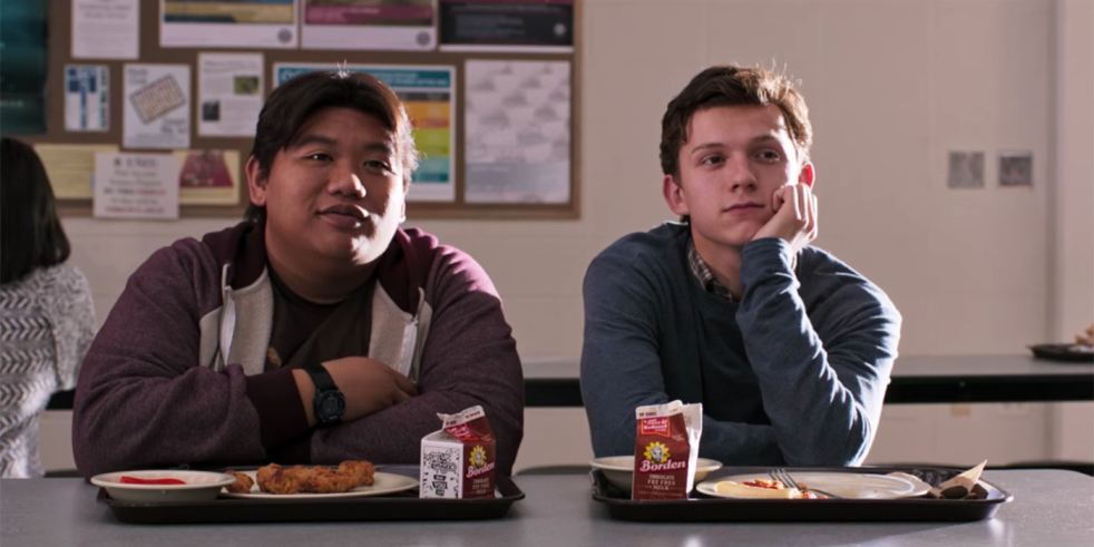 Ned Leeds (Jacob Batalon) and Peter Parker (Tom Holland) sitting at a lunch table in the school cafeteria. 