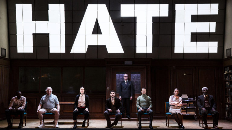 Photo of 1984 cast sitting on stage with HATE on a screen above them