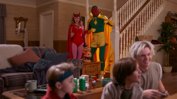 A still from the Disney+ show "WandaVision" featuring Wanda (Elizabeth Olsen) and Vision (Paul Bettany) waiting to go trick or treating with twins Billy (Julian Hilliard) and Tommy (Jett Klyne) while they play video games with Uncle Pietro (Evan Peters).
