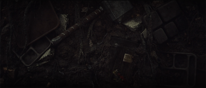 Mjolnir and a jar containing a frog dressed like Thor is buried underground in a still from the Disney+ series "Loki."