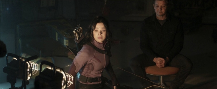 Kate Bishop (Hailee Steinfeld) looks on in dismay as the Tracksuit Mafia surround her and Clint Barton (Jeremy Renner) in a still from the Disney+ series "Hawkeye."
