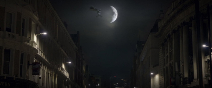 Moon Knight leaps across rooftops in front of a waning moon in a still from the upcoming Disney+ show "Moon Knight."