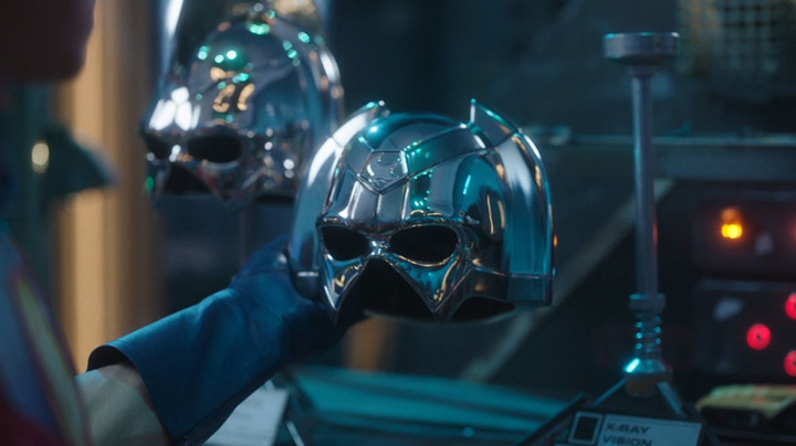 Peacemaker (John Cena) raids his father's workshop and takes some special helmets for himself in a still from HBOMax's "Peacemaker."
