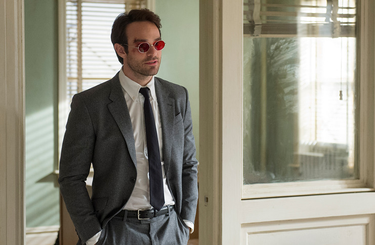 Charlie Cox as Matt Murdock wearing a gray suit, white shirt, black tie with amber glasses
