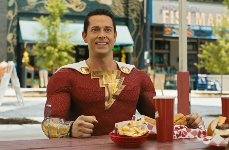 Zachary Levi in Shazam! Fury of the Gods sitting at a table with french fries and cheesesteak sandwich